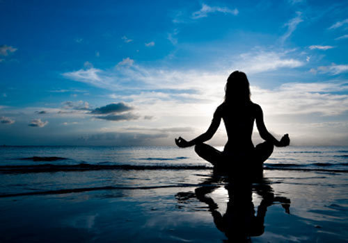 silhouette of lady meditating in lotus position on a beach